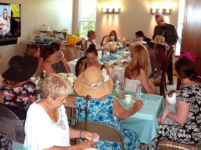 Mister Vibe reads palms of a large group of women seated in a living room.