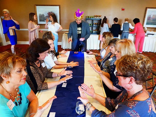 Standing at the head of a long banquet table seating eight women, Mister Vibe performs a group palm reading.