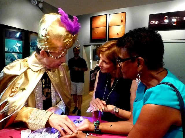 Wearing a gold suit and turban, Mister Vibe reads the palms of two women.