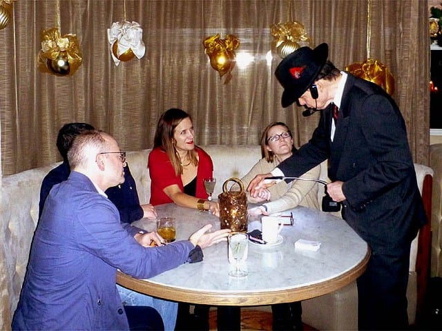 Mister Vibe reads the palms of a group of people seated around a table in a restaurant.
