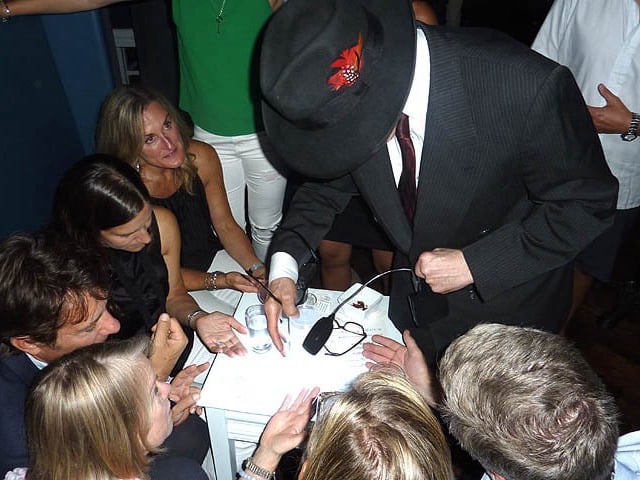 Mister Vibe reads the palms of a group of people seated around a table.