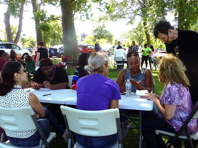 Seated group of people watching a woman get her palm read at a picnic table outdoors..