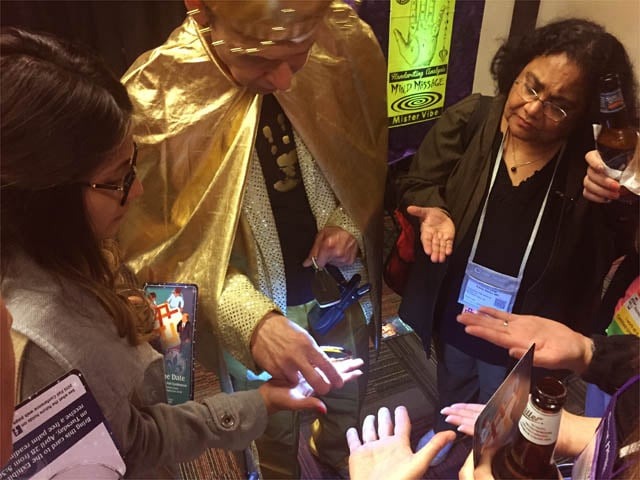 Mister Vibe reads the palms of a group of people at a trade show.