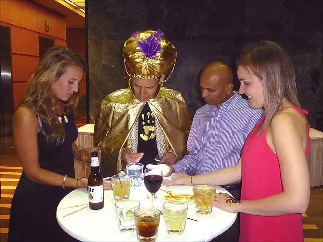 Mister Vibe reads the palms of a group of seated women who hold out their palms to him.