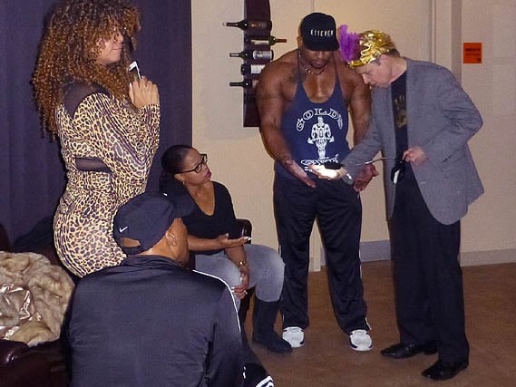 Mister Vibe reads the palm of a muscular Black man as other people watch.
