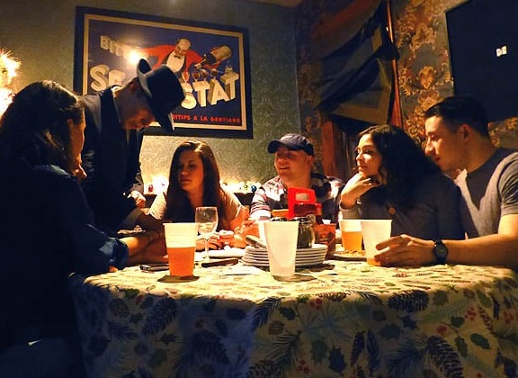 Mister Vibe reads the palms of a group of people seated around a table in a restaurant.