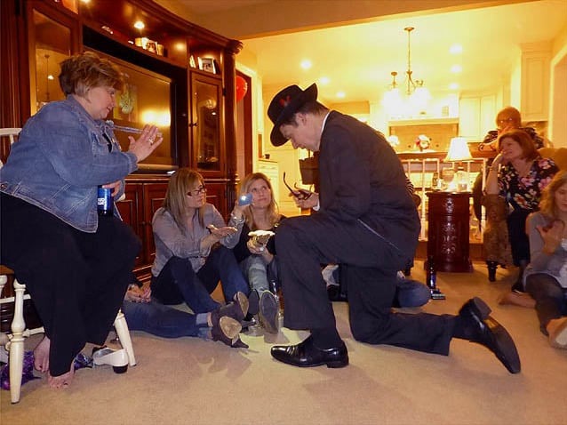 Mister Vibe kneels to read the palms of two women sitting on the floor in a living room.