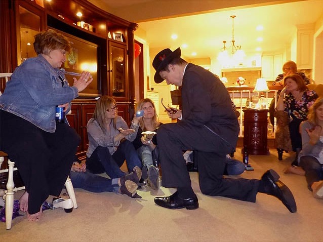 Mister Vibe kneels to read the palms of two women sitting on the floor in a living room.
