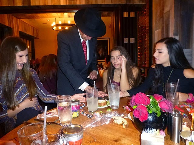 Mister Vibe reads palms of three seated teen girls at a restaurant.
